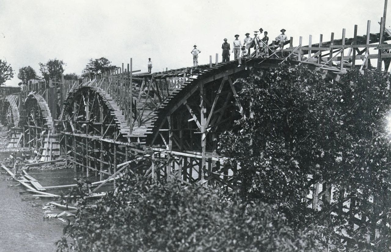 Historical black-and-white photo of the Interurban Bridge under construction in 1908, workers standing atop the wooden formwork